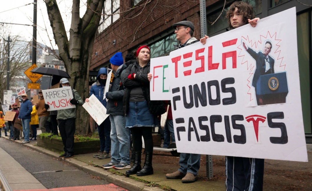 Manifestantes seguram cartazes durante um protesto no showroom da fabricante de carros elétricos Tesla em Seattle, Washington, EUA, em 15 de fevereiro de 2025