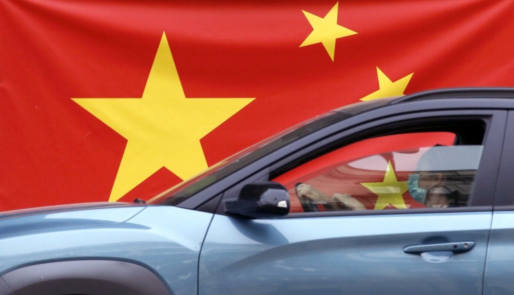 Nesta foto de 13 de abril de 2020, uma mulher usando máscara facial passa por uma bandeira chinesa colocada em uma rua